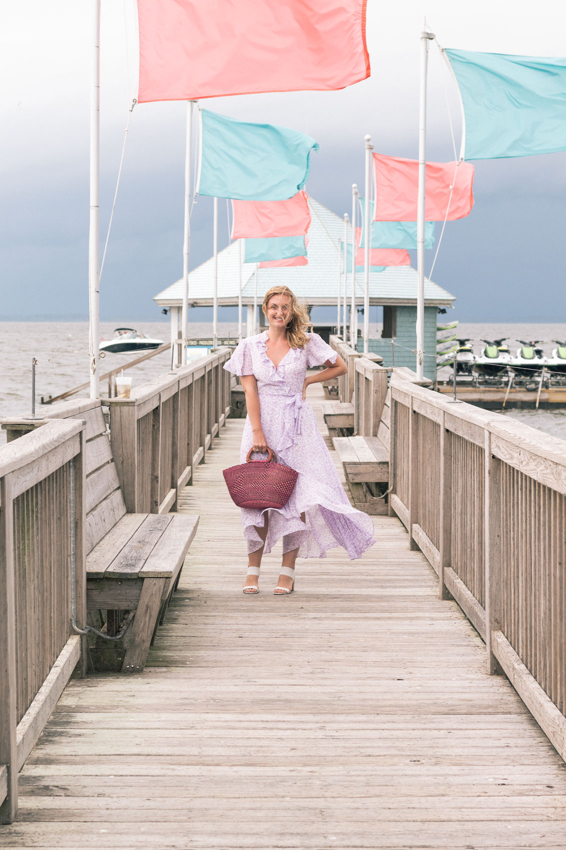 Allyn Lewis styles a purple faux wrap Gal Meets Glam Collection dress with block heels and a pink woven bag while on vacation in the Outer Banks, NC. 