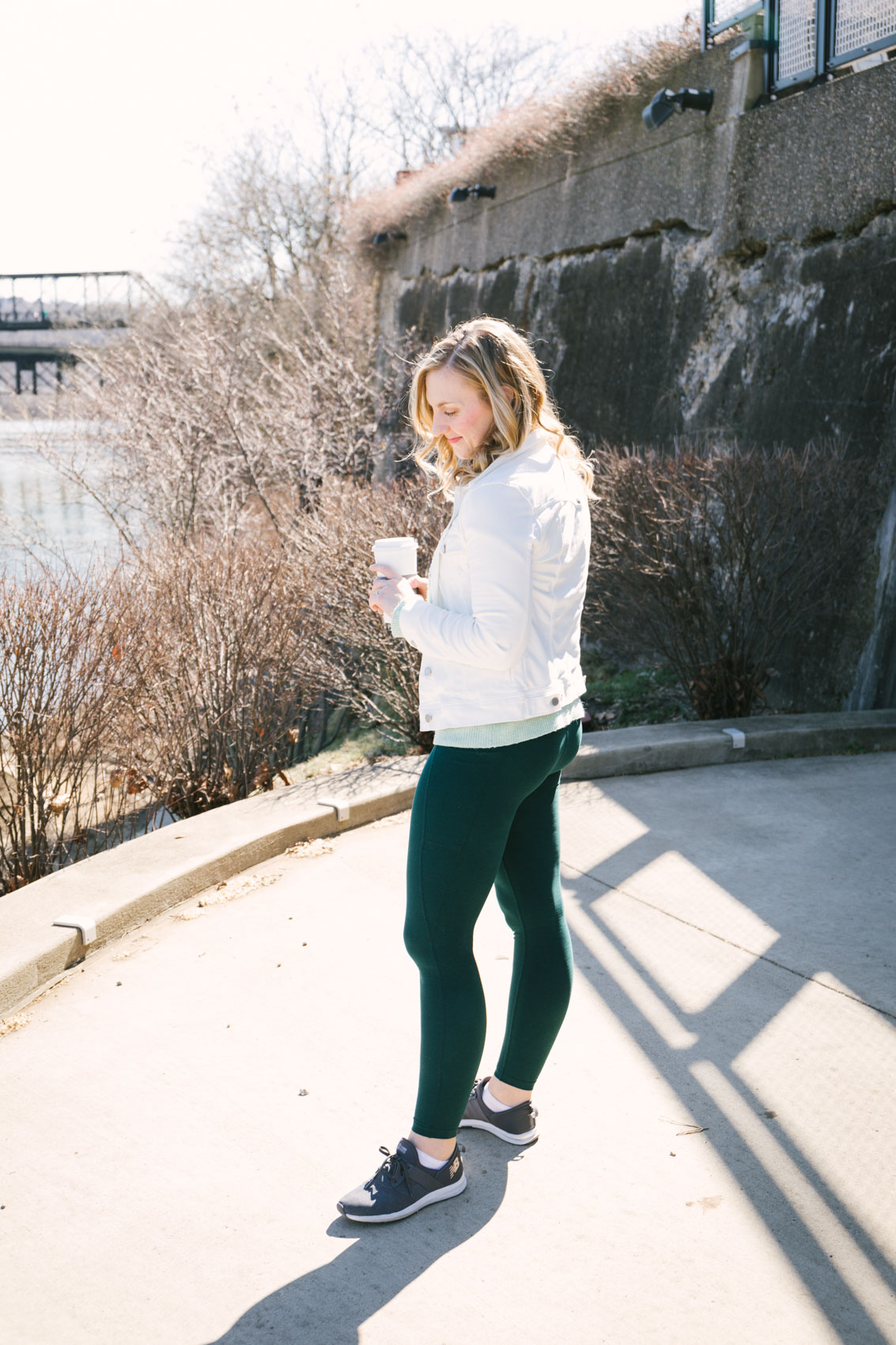 Allyn Lewis styles a cute athleisure outfit with beyond yoga leggings, a mint green sweater, white denim jacket and sneakers. 