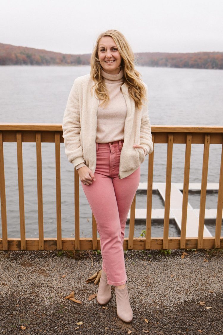 Allyn Lewis styles a beige winter outfit with a sherpa jacket, turtleneck sweater, pink jeans, and ankle boots.
