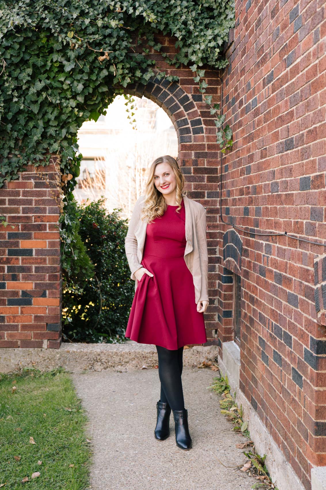 Allyn Lewis styles a red dress that as pockets with black tights, ankle boots, and a tan faux suede jacket for a classy winter outfit that can be work casually, holiday events, or Christmas parties. 