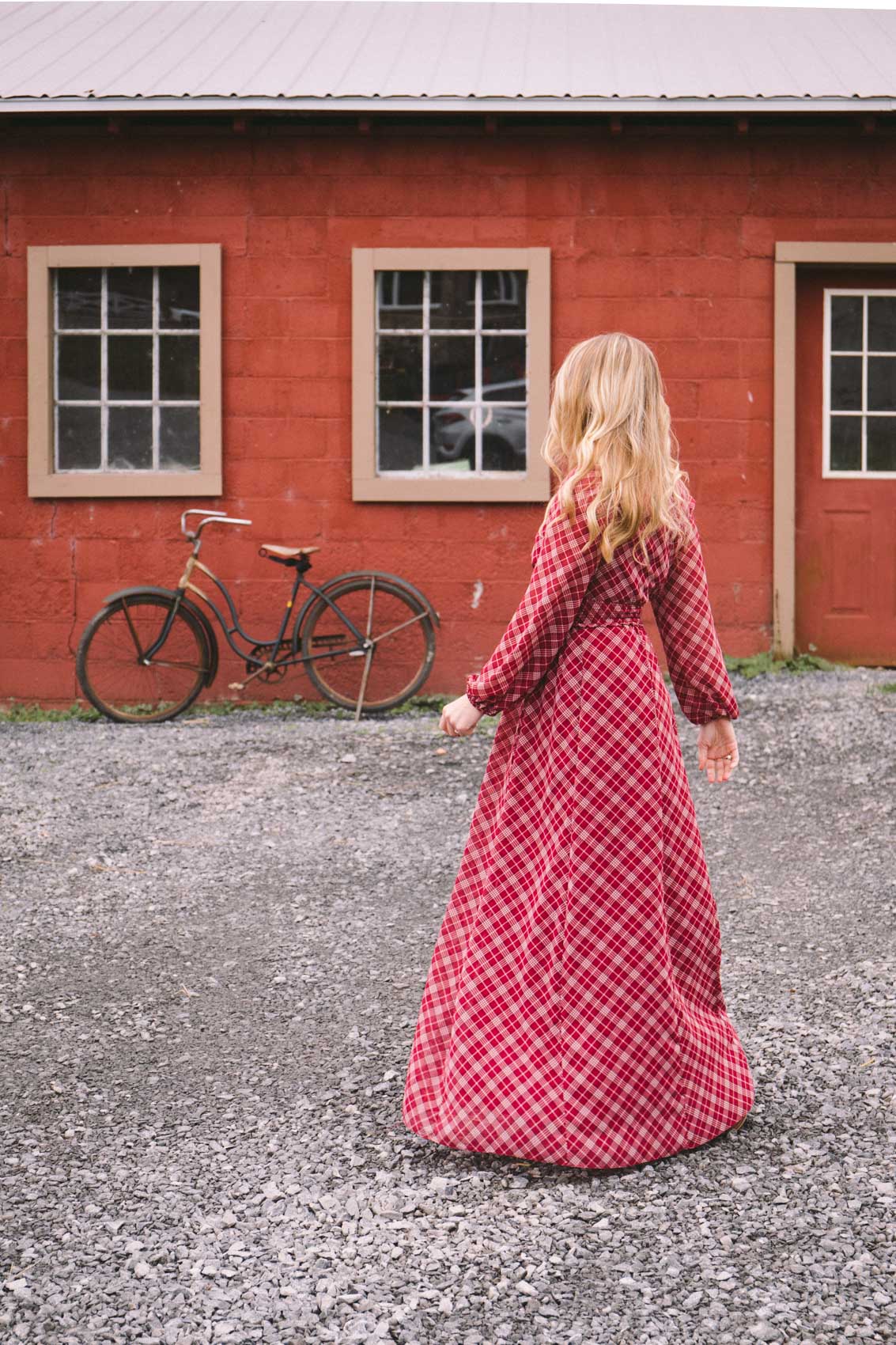 Woman twirling in a long sleeve red maxi dress in front of a red barn and vintage bicycle.