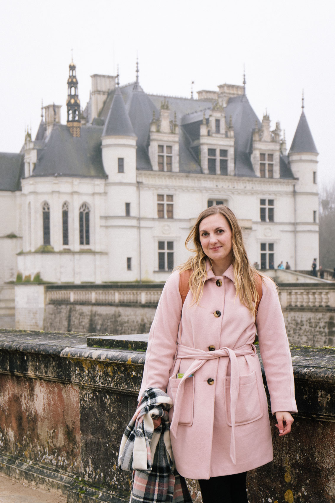 Women's winter outfit with a blush pink coat outside of the Château de Chenonceau in France