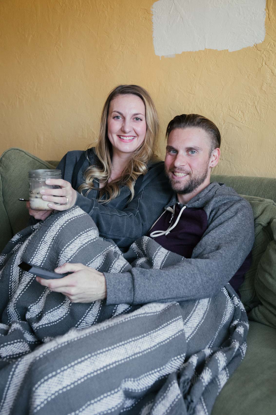 Lifestyle blogger Allyn Lewis snuggled up on the couch for movie night with husband Shaun Novak holding the Xfinity Voice Remote and ice cream 