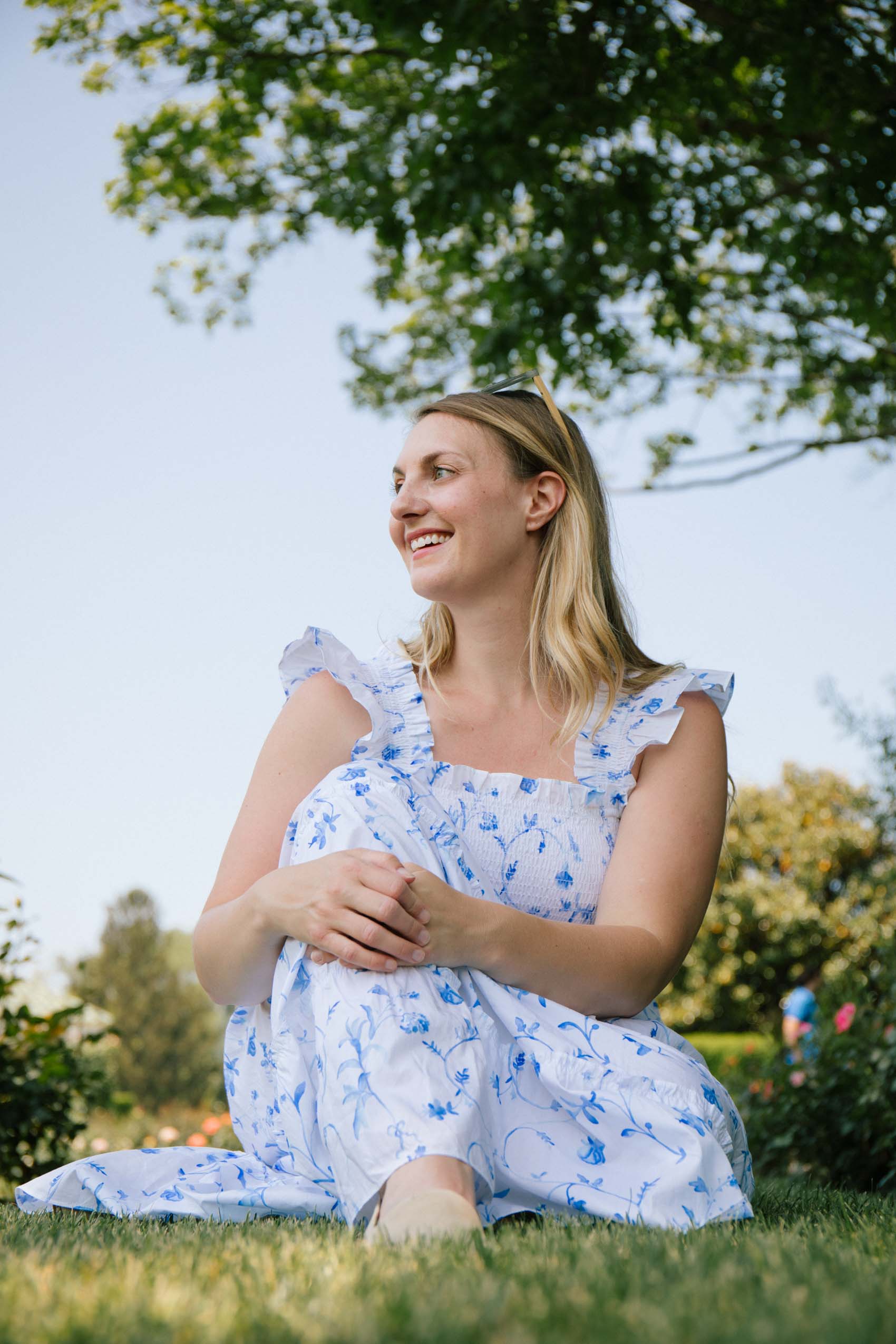 Women wearing a white cotton Hill House Nap Dress with blue floral print sitting in a garden. 