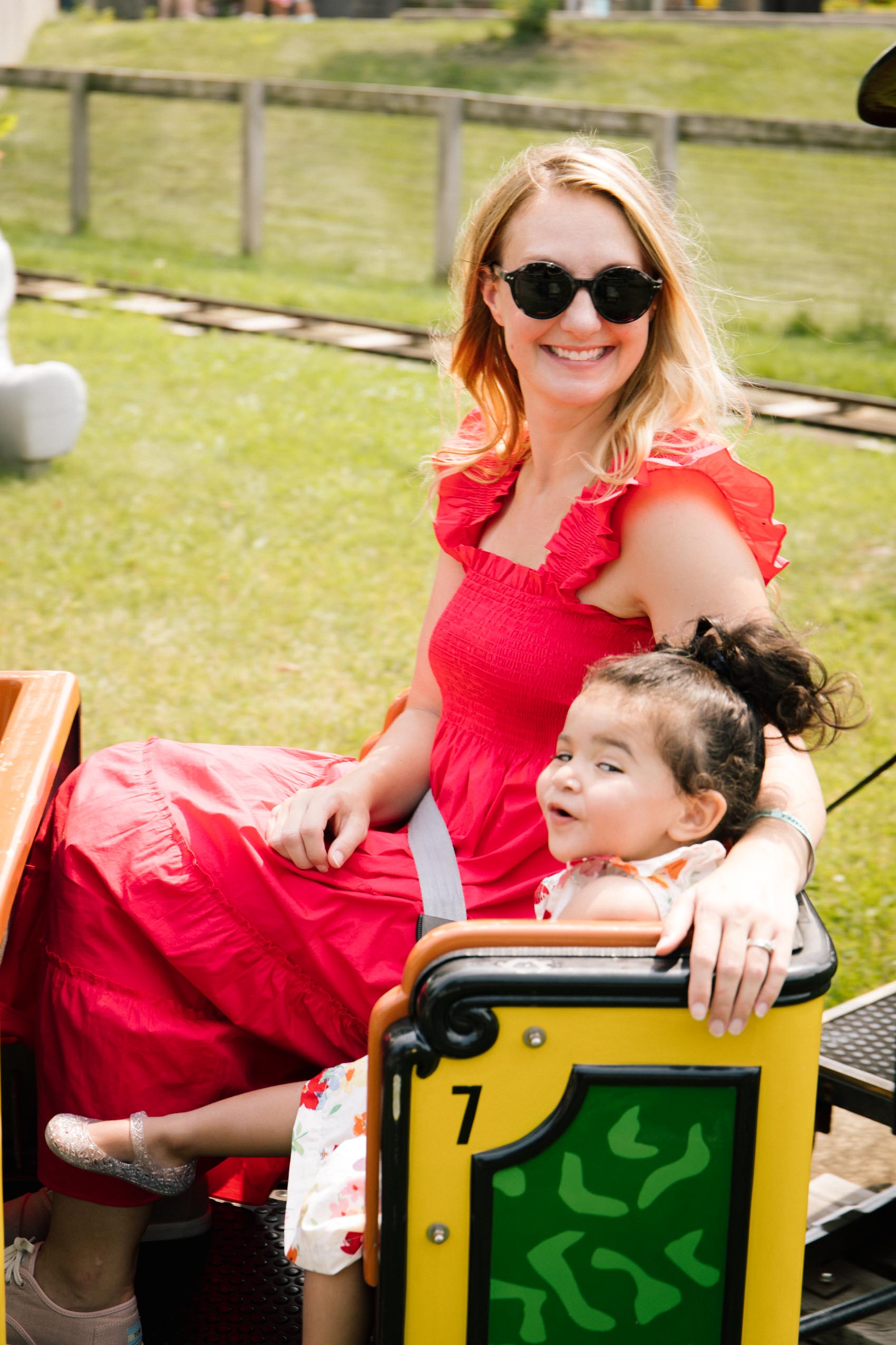 Woman wearing a red dress sitting next to a toddler on a kids' train ride