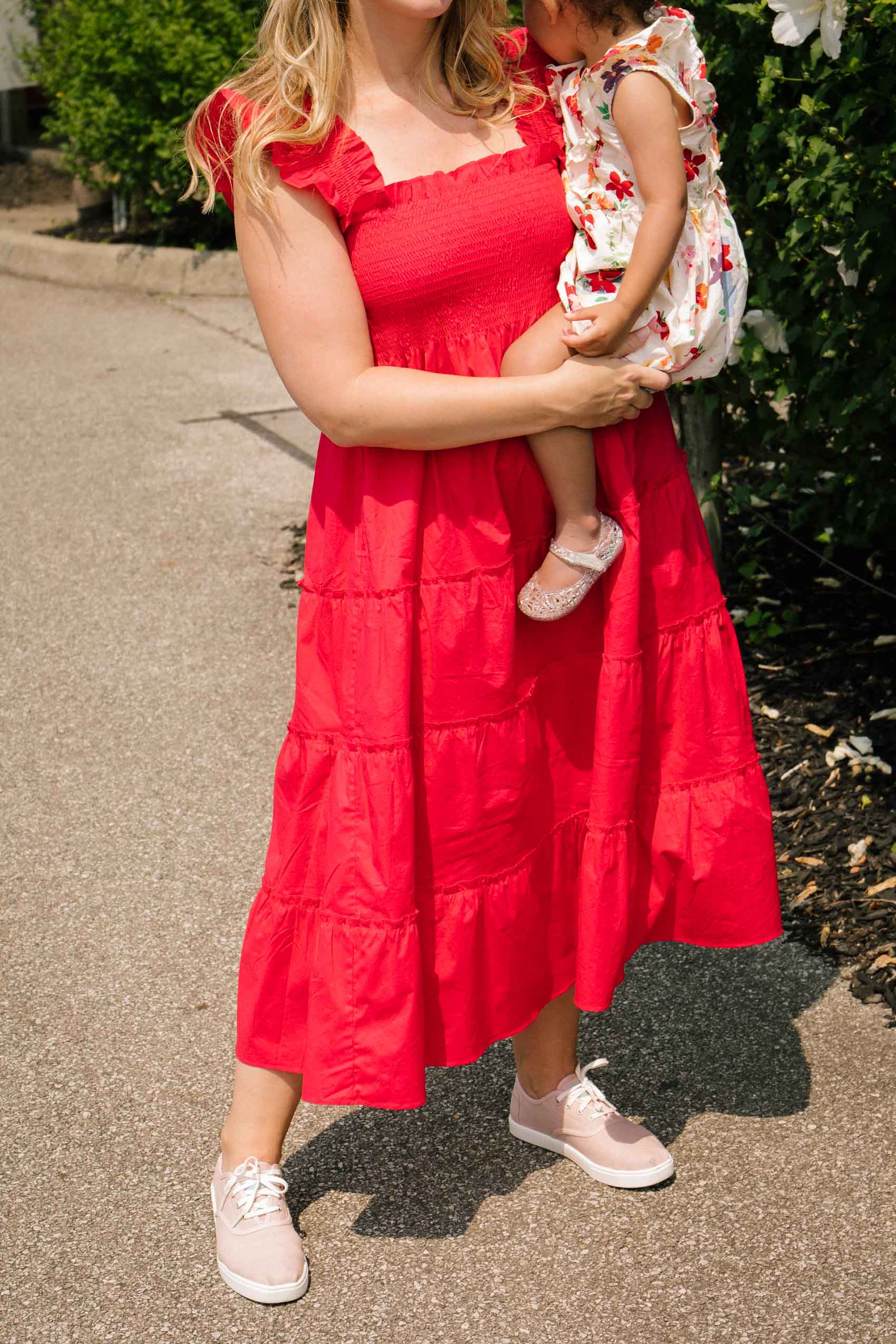 Woman wearing a red midi dress and pink sneakers while holding a toddler