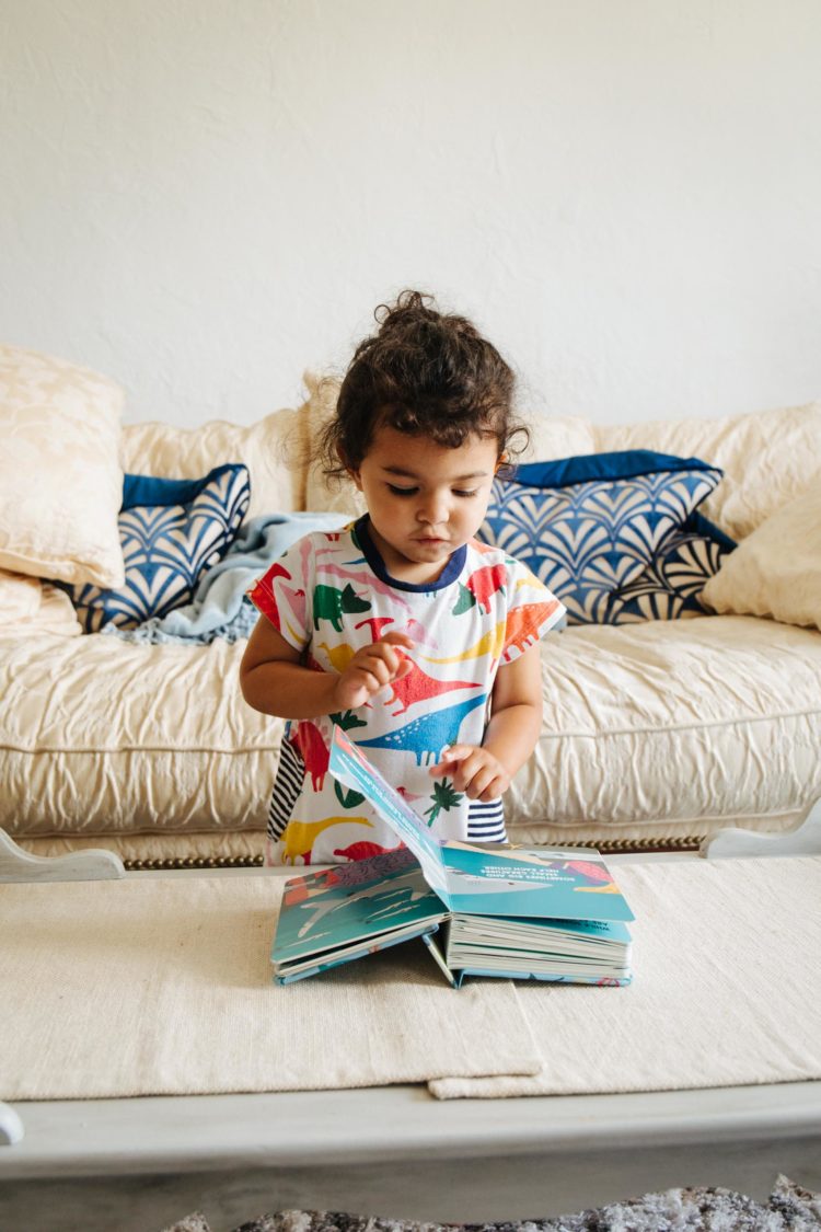 Toddler in a dinosaur tunic shirt reading a Sharkblock block book for kids