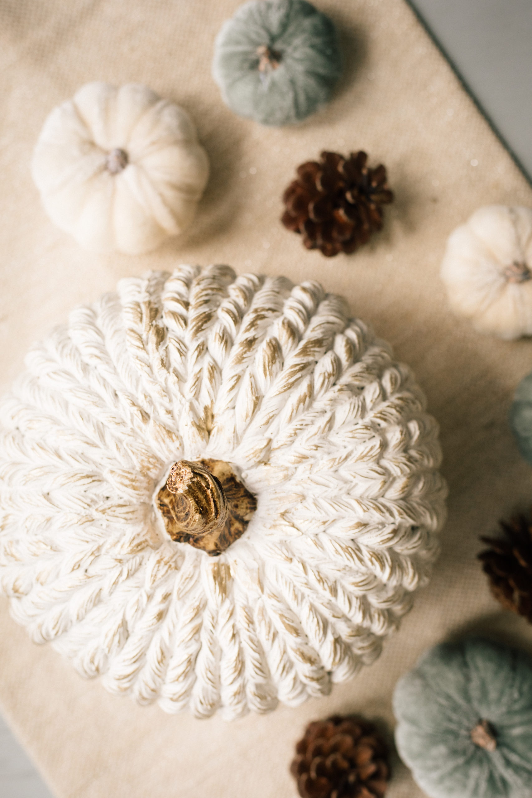 Classy fall Halloween decor with a large white and gold pumpkin surrounded by white and blue pumpkins and brown pine cones 