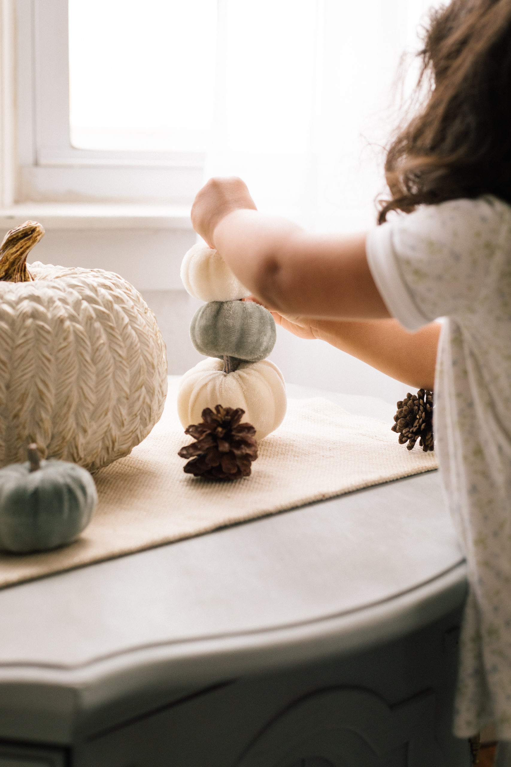 Toddler playing with small pumpkins and pinecones