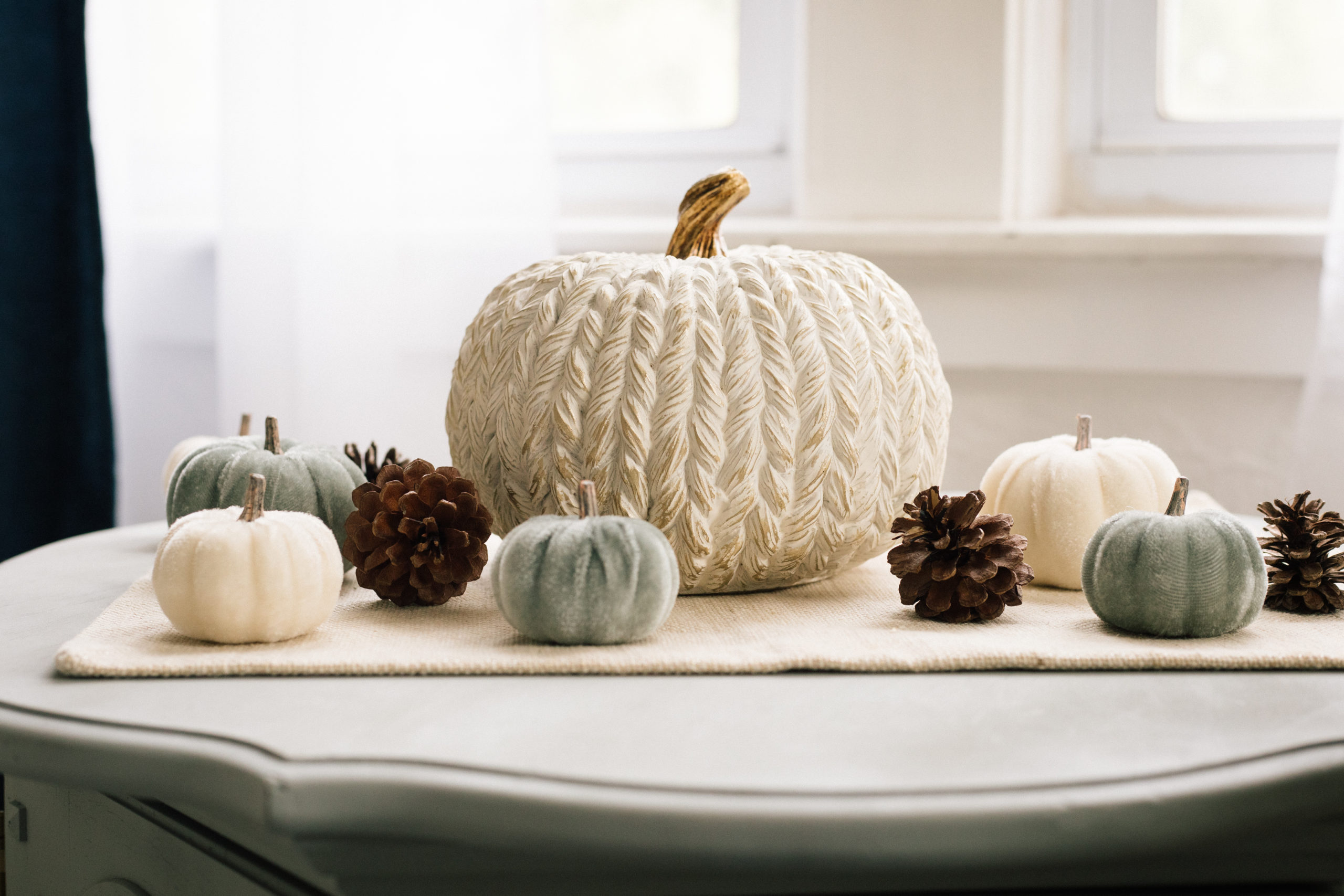 Classy fall decor in a living room including a large white and gold pumpkin surrounded by small pinecones and white and blue pumpkins 