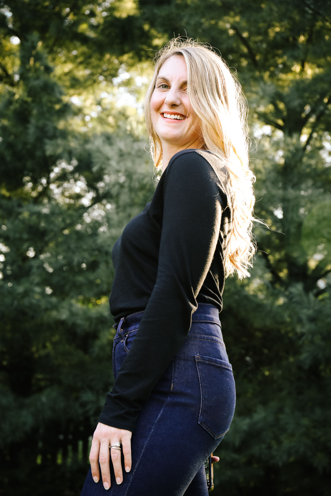 Woman smiling wearing a black long sleeve shirt and dark wash mom jeans from Mott & Bow clothing.