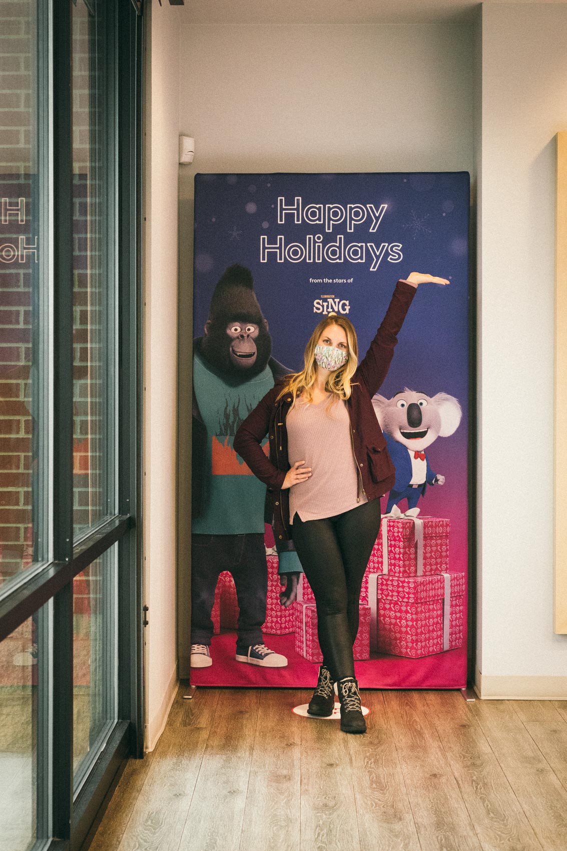 Woman standing in front of a "Happy Holiday" Sing 2 poster at an Xfinity retail store